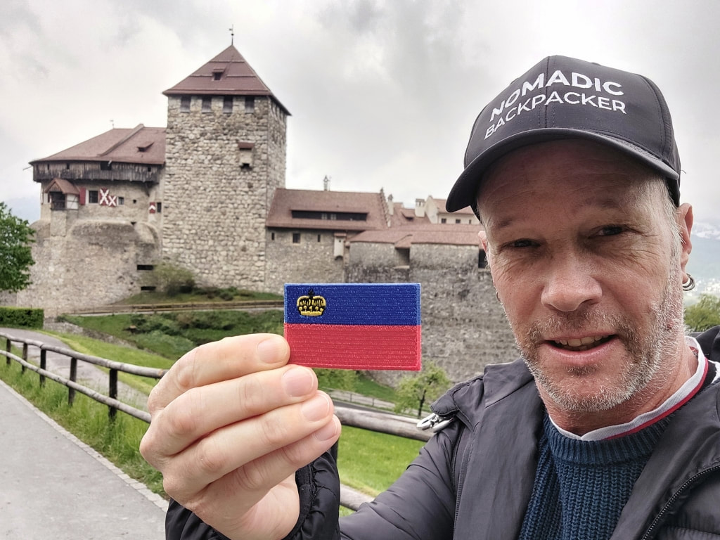 nomadic backpacker hold a small flag of the Principality of Liechtenstein in front of the castle 