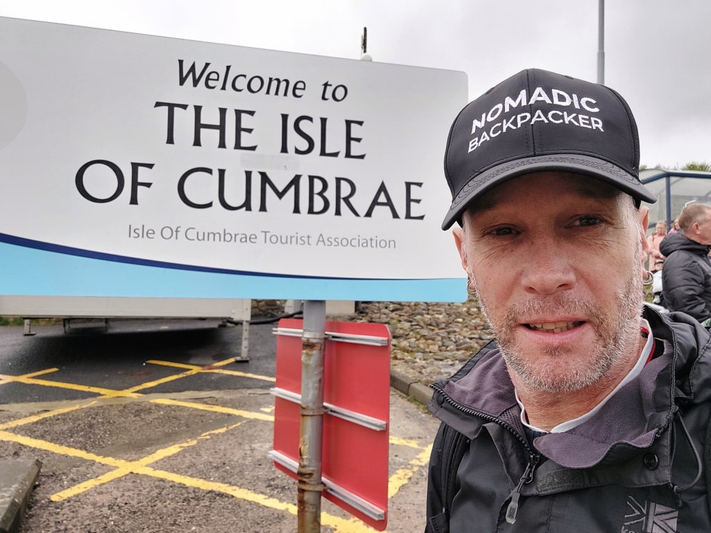 standing i front of the Welcome to the isle of Cumbrae sign