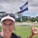 How to Cross the Peñas Blancas Border by Bus (Costa Rica to Nicaragua) Nomadic Backpacker at the Peñas Blancas Border between Costa Rica and Nicaragua with the flag behind