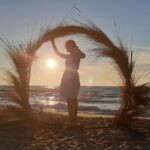 Lavdi Zymberi from Kosovo Girl Travels Discusses her 3 Favourite Countries Lavdi from Kosovo Girl Travels against a backdrop of a sandy beach and a sunset.